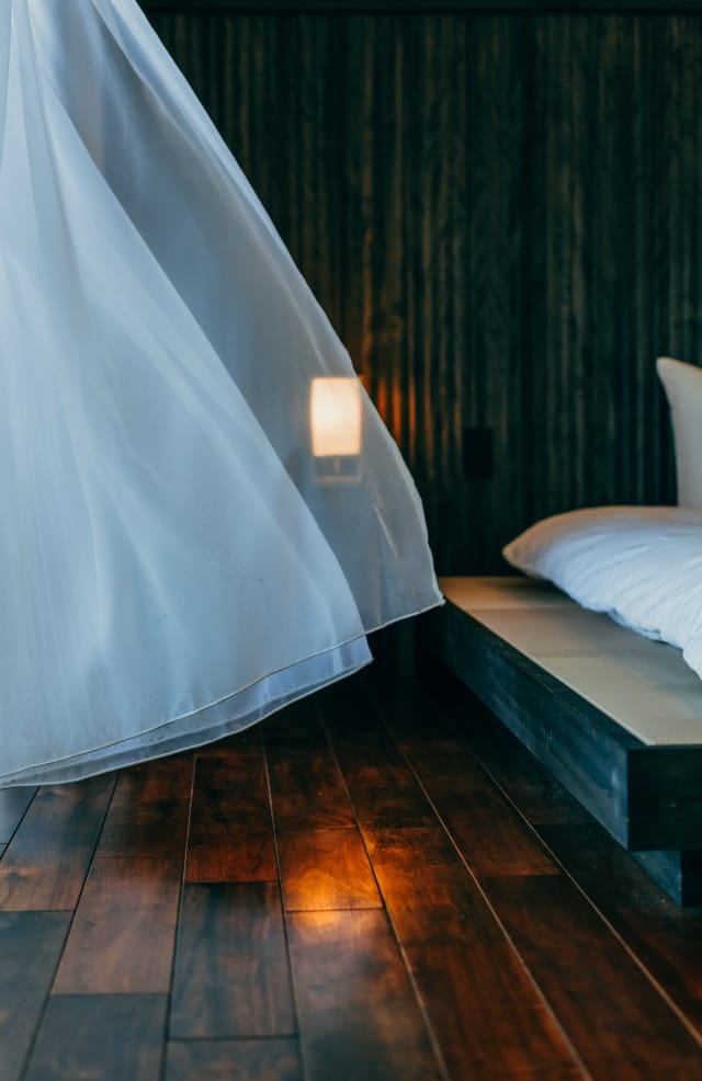 GOKKAI SEITEI bedroom with white canopy curtains and warm wood textures